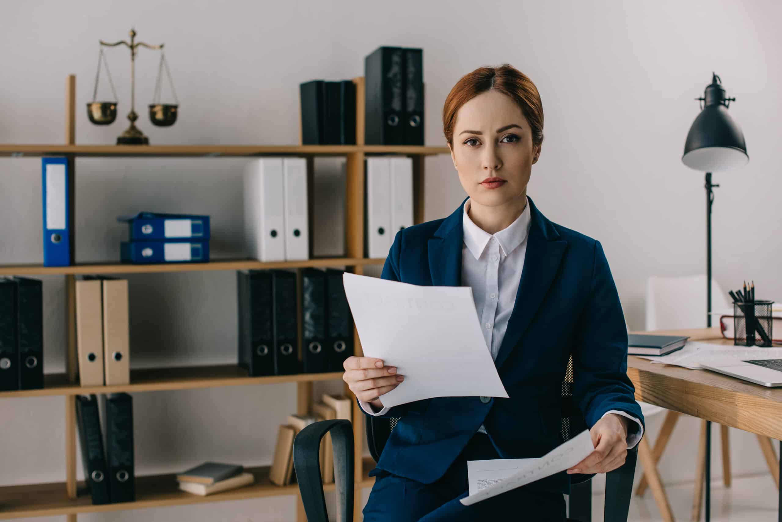 portrait of female lawyer in suit with documents in hands at workplace in office